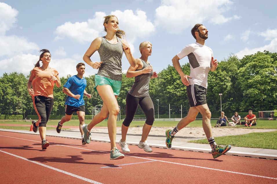 Fünf Erwachsene laufen gemeinsam auf einer Laufbahn im Stadion bei Sonnenschein.